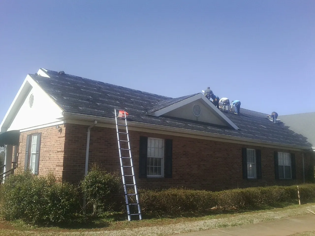 Crew tearing shingles off a brick ranch roof with a ladder set — Metal Roof Repair work by our crew in Wolf Creek