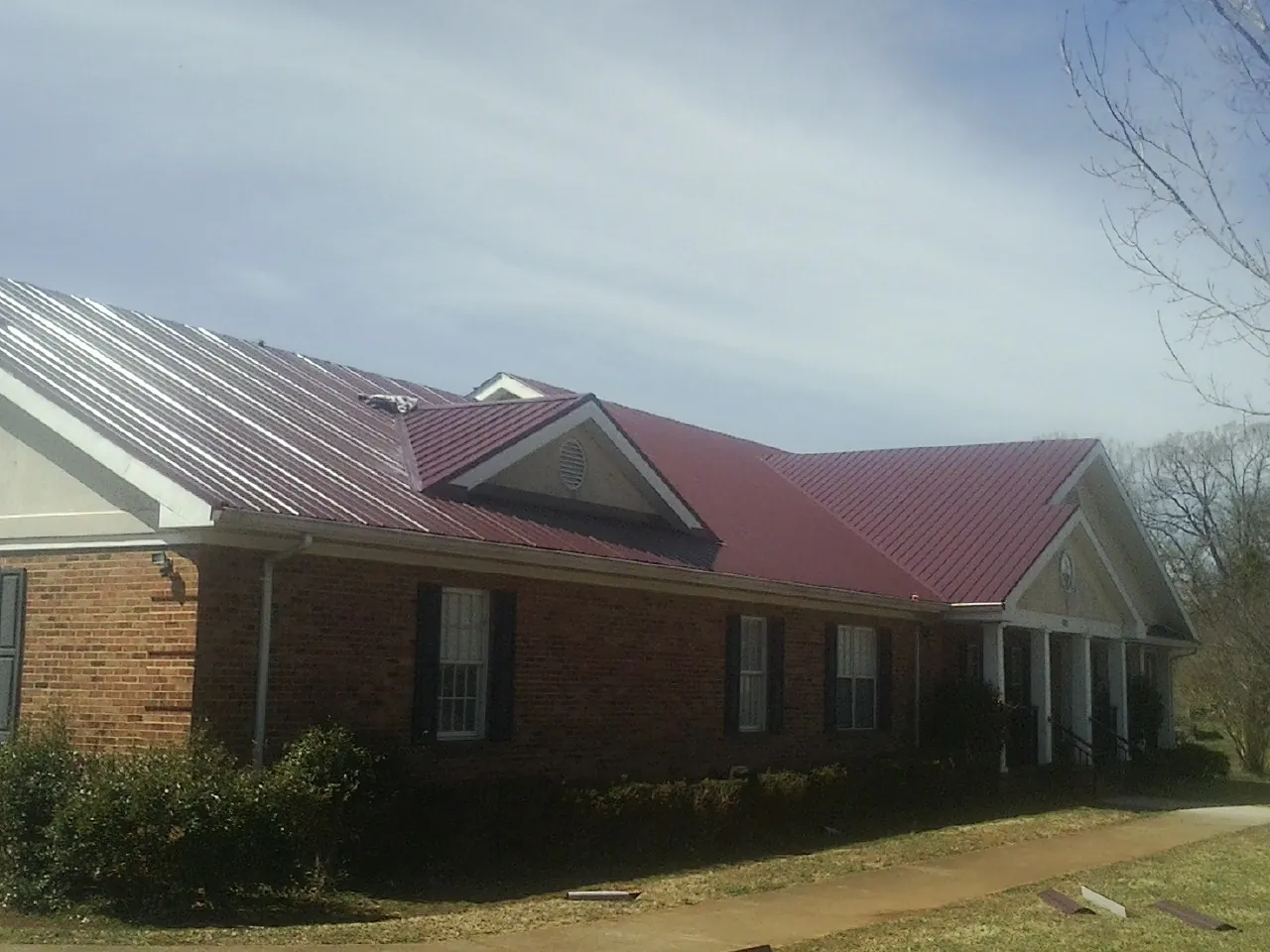Red metal roof with gabled entries on a long brick building, from a Hail Damage Roof Repair job in Wolf Creek