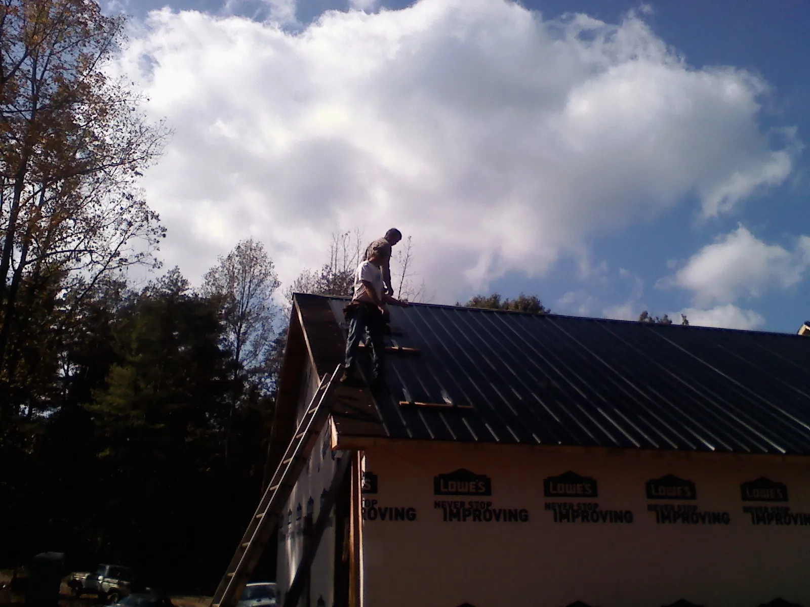 Roofer fastening dark metal panels high against a cloudy sky, from a Roof Inspection job in Wolf Creek